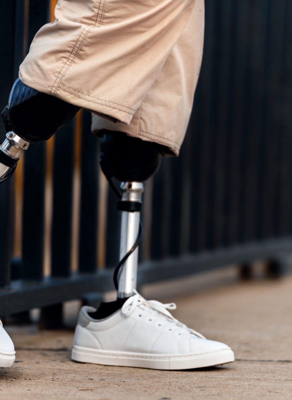 View of a man with prosthetic legs and white sneakers. Rested one foot on the fence